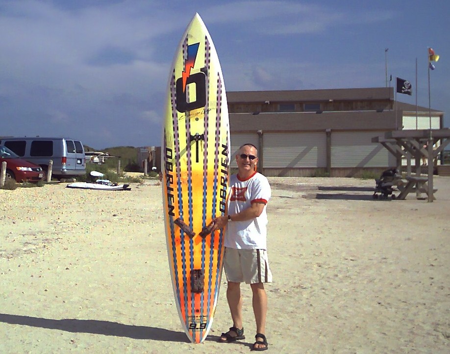 Dallas-Fort Worth windsurfer Mike Kimbro displaying the object of his affection, his 1989 O'Brien Epoxy Lite 9.9 Giant Slalom board in front of Worldwinds Windsurfing at Corpus Christi's Bird Island Basin sailing area.